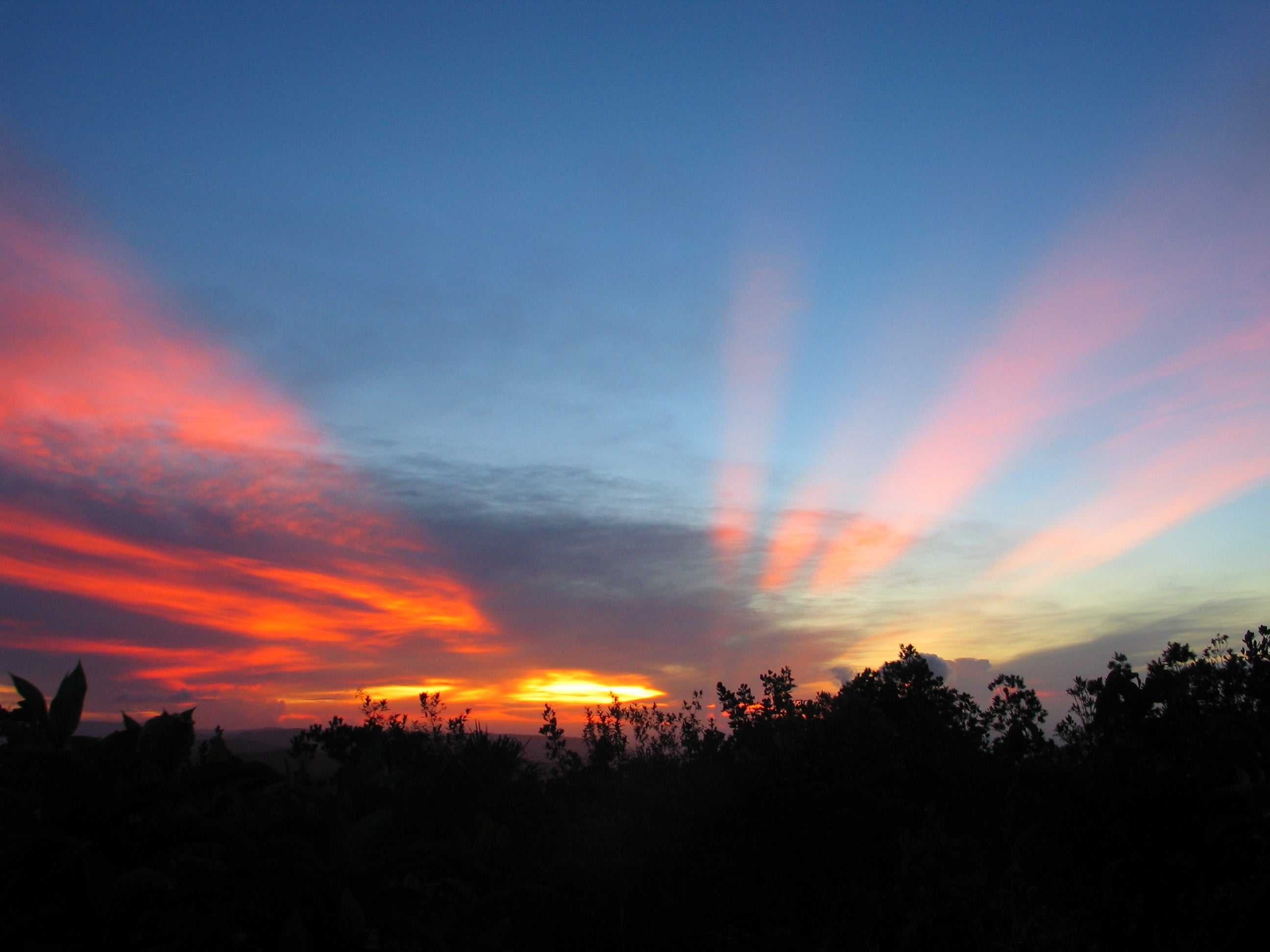 Sunset from Mount Maragaret, Belize. Red rays shine through clouds and the sun is brilliantly yellow against a deepening blue sky.